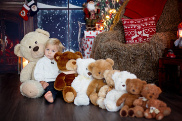 Obraz premium Cute toddler boy, sitting around many teddy bears on the floor, playing on Christmas