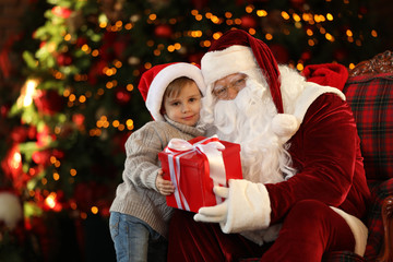 Fototapeta na wymiar Santa Claus and little boy with gift near Christmas tree indoors