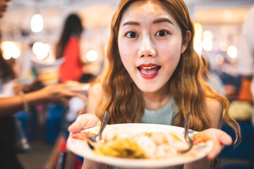 Traveler Asian blogger women travel in Bangkok, Thailand, beautiful female using Women travel in Thailand concept.Woman enjoy her bowl of noodles in outdoor night market in Bangkok city