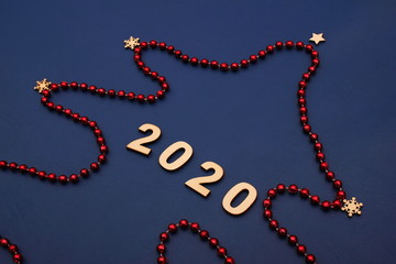 2020 Happy New Year. A Christmas tree made of red Christmas beads is laid out on a blue background.