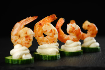Delicious sauteed shrimp on cream cheese and sliced cucumber. black background closeup	
