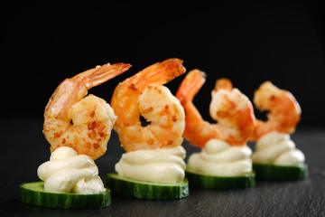Delicious sauteed shrimp on cream cheese and sliced cucumber. black background closeup