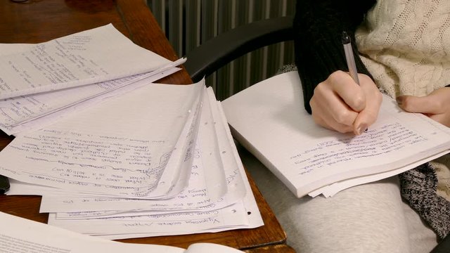 Close dolly shot of a young woman student&rsquo;s hand using a pen to write assignment notes.
