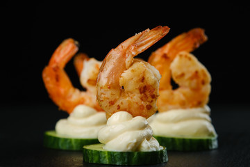 Delicious sauteed shrimp on cream cheese and sliced cucumber. black background closeup	