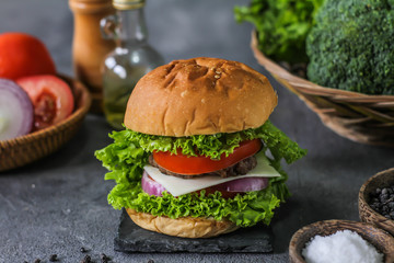 Photo of fresh burger on wooden cutting board on dark background..Homemade hamburger with beef, onion, tomato, lettuce and cheese. Homemade fast food. Dark textured background. Copy space. Image.