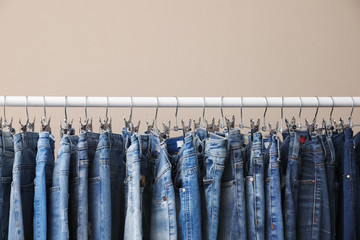 Rack with stylish jeans on beige background, closeup