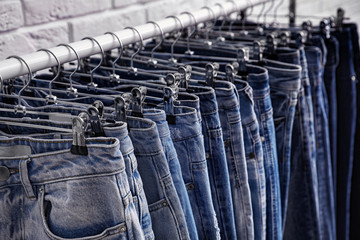 Fototapeta premium Rack with stylish jeans near brick wall, closeup