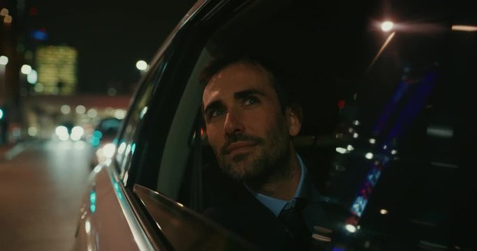 Slow motion close up of young handsome businessman looking outside during traveling in modern car with a driver in center of the city by night.Shot in 8K.Concept of business,success, traveling luxury 