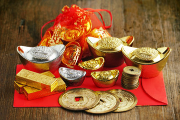 Coin and gold and silver bars decorate on red envelope on wood background.