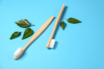 Two wooden bamboo eco friendly toothbrushes and green leaf on blue background. Dental care and zero waste concept. Flat lay, top view, copy space