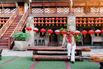 Happy muslim Woman tourist sitting on a table in a Chinese house atmosphere, Asian woman  in holiday. Travel concept. Chinese theme.