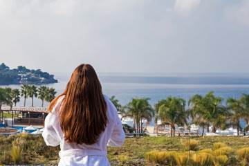 Fototapeta na wymiar Woman in bathrobe standing on the balcony of luxury hotel and looking on the sea