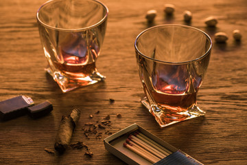 Glasses of brandy with cigar, lighter and pistachios on wooden table