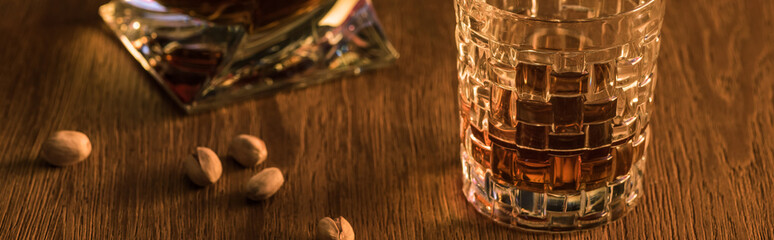 Glass of brandy with pistachios and decanter on wooden table, panoramic shot