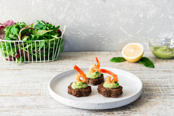 Canapes with avocado mousse and spicy shrimp on brown bread