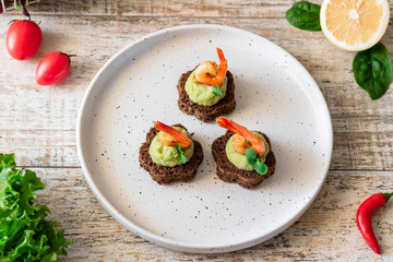 Canapes with avocado mousse and spicy shrimp on brown bread