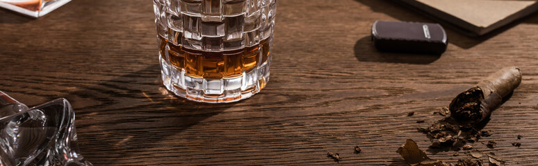 Glass of brandy with cigar, lighter and book on wooden table, panoramic shot