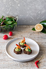 Canapes with avocado mousse and spicy shrimp on brown bread