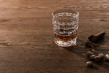 Glass of brandy with cigar and pistachios on wooden table
