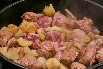 Frying the raw beef and the onions in a cauldron to prepare the Hungarian cauldron goulash.