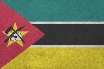 Mozambique flag depicted in bright paint colors on old relief plastering wall. Textured banner on...
