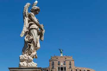 Statue on the pont Sant'Angelo or bridge of Angels in rome against a blue sky with a seagull and the Castle of Angles or Castel d'Angleo in the background