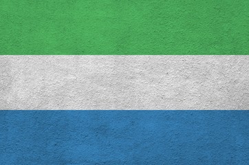 Sierra Leone flag depicted in bright paint colors on old relief plastering wall. Textured banner on...