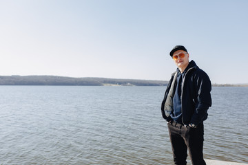 stylish young boy in orange glasses, jacket and cap, walk around the lake in spring or autumn