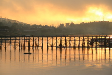 A little boat and wooden bridge with mountain landscape over the river at Sunrise in Thailand.