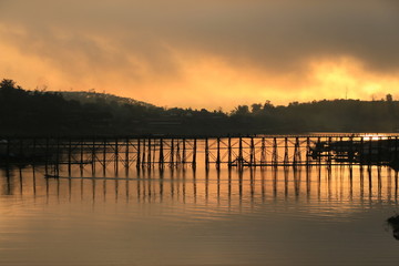 A wooden bridge with mountain landscape over the river at Sunrise in Thailand.
