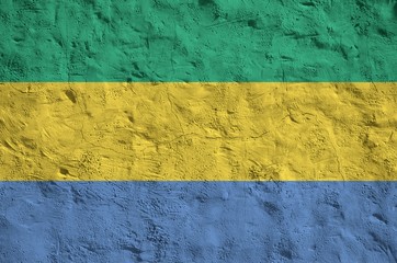Gabon flag depicted in bright paint colors on old relief plastering wall. Textured banner on rough...