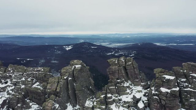 Aerial view; drone flies over rocky peaks of mountain ridge Otkliknoy Greben'; dangerous climbing route for tourists in winter; snow-covered stone and boulders; panorama of Ural mountains in foggy day