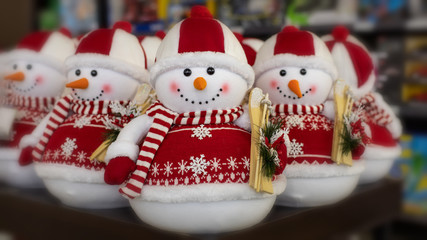 A toy snowman in a red sweater and hat holding wooden skis in his hands. New Year decorations, Christmas holiday toys. Greeting card with snowmen