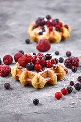 Fresh small round waffles topped with fruits like blueberry and cranberry and powdered sugar 