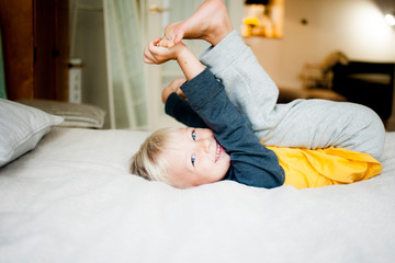 A boy of five years old is lying in bed on his back smiling, looking at the camera.