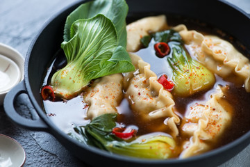 Close-up of panasian dumpling soup with pak-choi in a cast-iron pan, selective focus