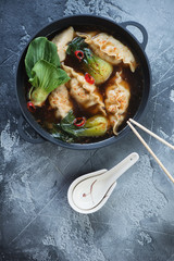 Cast-iron pan with dumplings and pak-choi in miso broth, top view on a grey weathered concrete background, vertical shot