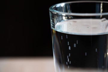 Glass with water on a black background. Bubbles rise up. A glass mug filled with water stands on a wooden table. A cup of water