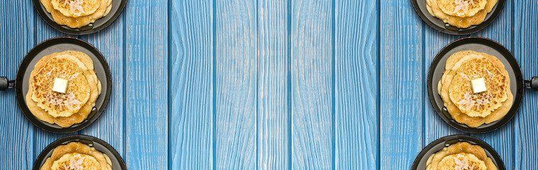 Hot delicious pancakes in frying pans on blue wooden table. Pancake week. Panoramic banner.
