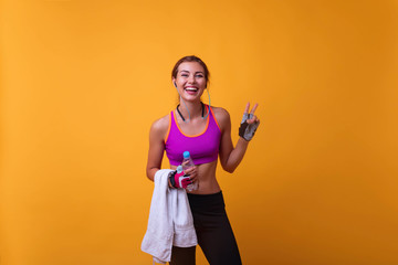 Happy young woman in sports clothing smiling. Muscular fitness model on yellow background looking...