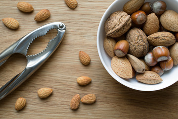 Assorted nuts in white bowl on wooden surface.