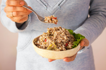 Woman hands holds cooked buckwheat porridge in bowl.