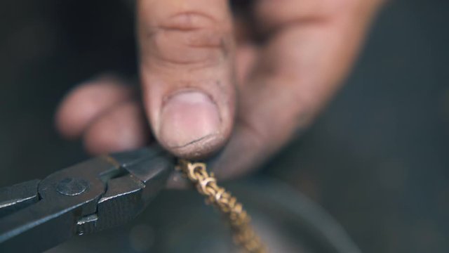 CU: goldsmith cuts leftover parts from shiny gold chain with old pliers on blurred background extreme close view