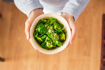 Woman hands holds green salad with spinach.