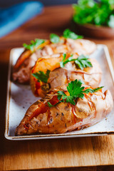 Baked three sweet potatoes with fresh parsley on a white ceramic dish. Healthy veggie dinner or lunch.
