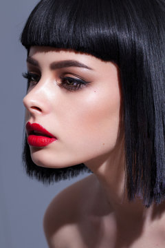 Profile photo of a young beautiful brunette model with colorful professional make up, bob hair cut and red lips
