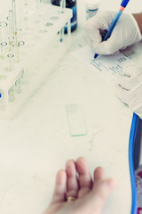 Closeup of blood sampling from finger, lab technician and patient hands.