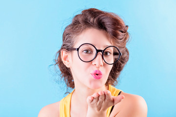 Beautiful brunette in a yellow top and fashion glasses sends an air kiss, beauty concept, blue...
