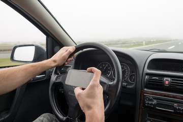 Use of smartphone in car. Man using phone while driving in fog on highway.