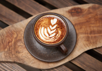 A beautiful creamy brown warm fresh cappuccino coffee cup, full of creamy coffee, served in a wooden rustic brown coffee shop with coffee art. Organic fair trade coffee photographed from above top 